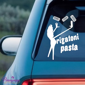 May include: White vinyl car decal featuring a stylized figure juggling rigatoni pasta. The text "rigatoni pasta" is below the figure. The decal is applied to a car window, with the car's blue paint visible.