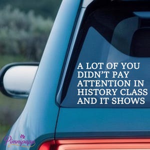 May include: A blue car window sticker with white text that reads: "A LOT OF YOU DIDN'T PAY ATTENTION IN HISTORY CLASS AND IT SHOWS." The sticker is on the rear window of a blue car.