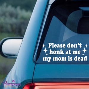 May include: White vinyl car decal with the text "Please don't honk at me my mom is dead" in a playful font, with star accents. The decal is applied to the rear window of a teal car.