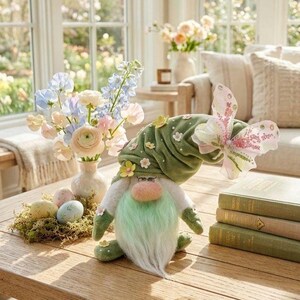 Puede incluir: Un gnomo de Pascua caprichoso con un sombrero verde adornado con flores y una mariposa. El gnomo tiene una larga barba blanca y una nariz rosada. Huevos de Pascua decorativos y un jarrón de flores también están sobre la mesa.