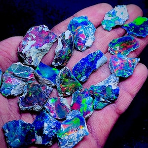 May include: A collection of rough opal gemstones, showcasing vibrant colors of blue, green, red, and purple. The opals are held in a hand, revealing their natural, unpolished state. The stones vary in size and shape, with a mix of colors.