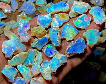 May include: A selection of raw opal gemstones, displaying a vibrant array of colours. The opals show a mix of blues, greens, and flashes of other hues. The rough texture of the stones is visible, highlighting their natural state.
