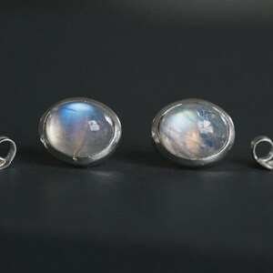 May include: A pair of round, silver-toned stud earrings with iridescent, moonstone-like centers. Two matching earring backs are also visible. The earrings are set against a dark background, highlighting their reflective qualities.