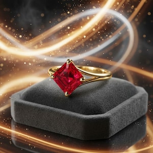 Puede incluir: Un anillo de oro con una piedra preciosa roja de corte cuadrado sujeta por cuatro garras. La banda presenta un diseño de brazo dividido que se estrecha hacia el engaste, mostrando un acabado metálico pulido que resalta el color rojo intenso.