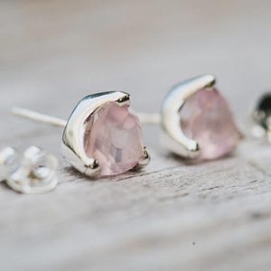 Op de afbeelding: Close-up van twee zilveren oorstekers met lichtroze, druppelvormige edelstenen. De oorbellen zijn gezet in een zilveren bezel en hebben een post-sluiting. Een bijpassende oorbelachterkant is ook zichtbaar.