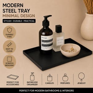 Peut inclure: Un plateau rectangulaire en acier noir contenant un flacon pompe en verre ambré étiqueté Aesop, un flacon de parfum en verre transparent étiqueté Zara Home et un petit bol en céramique beige avec des bijoux dorés, disposés sur une surface.