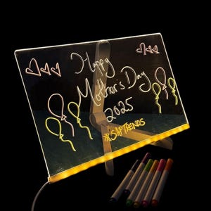 May include: A clear acrylic light-up drawing board with a white stand. The board has a yellow light around the edge and is lit up from behind. The board has a message written on it in pink and yellow neon markers that says "Happy Mother's Day 2023 #SHAPTRENDS". There are six multi-coloured markers next to the board.