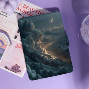 May include: A tablet case featuring a celestial design with a crescent moon and dramatic cloud formations. The case is predominantly dark blue and gray, with a touch of golden light. The text "A BEAUTIFUL WORLD" is visible on a nearby paper.