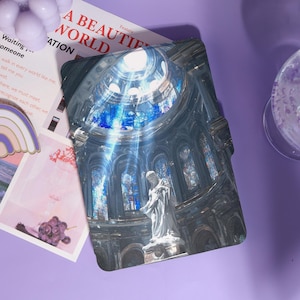 May include: A decorative print featuring a detailed illustration of a cathedral interior with a statue. The print has a blue and gray color scheme, with the text "A BEAUTIFUL WORLD" visible. The print is on a purple surface.