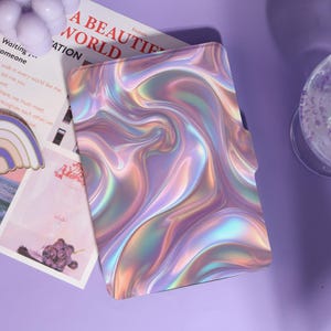 May include: A tablet case with a swirling, iridescent design in shades of purple, pink, and gold. The case has a smooth, glossy finish. The text "A BEAUTIFUL WORLD" is partially visible on a paper next to the case.