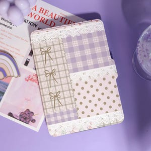 May include: A decorative tablet case with a patchwork design. The case features sections of plaid, polka dots, and bows in shades of lavender, pink, and beige, trimmed with white lace. The text "A BEAUTIFUL WORLD" is visible.