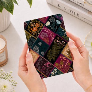 May include: A rectangular e-reader cover featuring a dark patchwork design with various floral and botanical illustrations in shades of deep magenta, forest green, mustard yellow, and black, with intricate white paisley and leaf patterns.