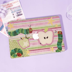 Peut inclure: Un autocollant pour ordinateur portable avec un motif coloré à rayures horizontales dans des tons de rose, vert et blanc. Le design présente des illustrations de chenilles vertes, d'une pomme coupée, d'une pomme entière et d'étoiles jaunes.