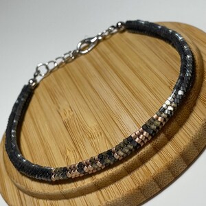 Könnte beinhalten: Ein Armband aus schwarzen, silbernen und kupfernen Perlen mit einem silbernen Verschluss.