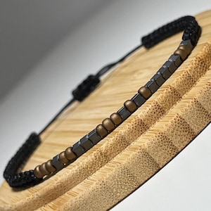 May include: A black cord bracelet with small, square, black and gold beads.