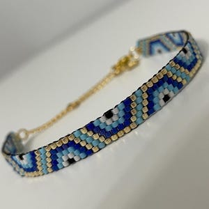 Könnte beinhalten: Ein blaues und goldenes Perlenarmband mit einem Muster aus bösen Augen. Das Armband hat einen goldenen Kettenverschluss.