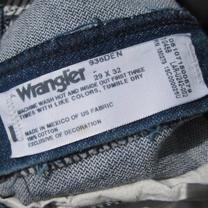 May include: Close-up of a denim Wrangler jeans label. The label displays the brand name, size 29 x 32, and care instructions. The jeans are made of 100% cotton and manufactured in Mexico.
