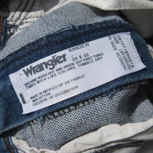May include: Close-up of the inside label of Wrangler denim jeans. The label is white with black text, including the brand name, size 29 x 32, and care instructions. The jeans are a medium blue wash.