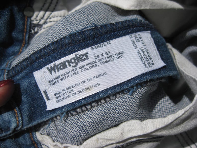 May include: Close-up of the inside label of Wrangler denim jeans. The label is white with black text, including the brand name, size 29 x 32, and care instructions. The jeans are a medium blue wash.