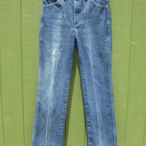 May include: Light blue denim jeans with a classic straight leg fit. The jeans have a faded wash and feature standard five-pocket styling, a button and zip closure, and belt loops. The jeans are hanging on a white hanger.