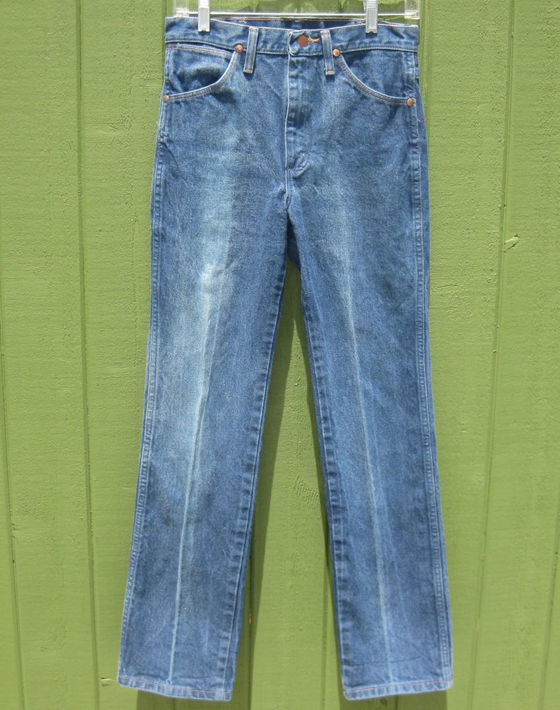 May include: Light blue denim jeans with a classic straight leg fit. The jeans have a faded wash and feature standard five-pocket styling, a button and zip closure, and belt loops. The jeans are hanging on a white hanger.