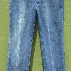 May include: Blue denim jeans with a classic five-pocket design. The jeans have a straight leg cut and are hanging on a metal hanger. The denim has a faded appearance, with lighter areas on the front of the legs.