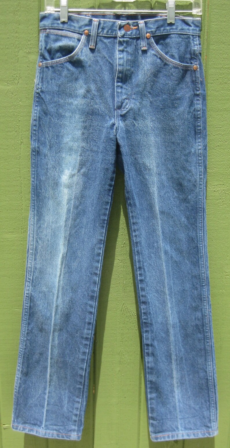 May include: Blue denim jeans with a classic five-pocket design. The jeans have a straight leg cut and are hanging on a metal hanger. The denim has a faded appearance, with lighter areas on the front of the legs.
