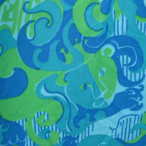 May include: Close-up of a fabric with a repeating pattern in shades of blue and green. The design features swirling shapes and stylized animal figures against a white background with vertical stripes. The fabric has a textured appearance.