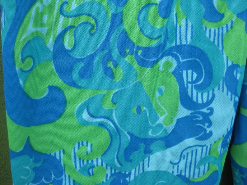 May include: Close-up of a fabric with a repeating pattern in shades of blue and green. The design features swirling shapes and stylized animal figures against a white background with vertical stripes. The fabric has a textured appearance.