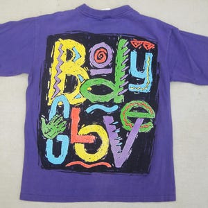 May include: A purple t-shirt with a colorful graphic design. The design features the words "Body Glove" in a variety of bright colors, including yellow, green, orange, and blue, set against a black background.