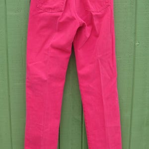Peut inclure: Un jean en denim rose vif suspendu &agrave; un cintre en m&eacute;tal. Le jean a deux poches arri&egrave;re, un patch en cuir marron et des rivets dor&eacute;s. Le jean est d'une couleur vive et unie et semble &ecirc;tre vintage.