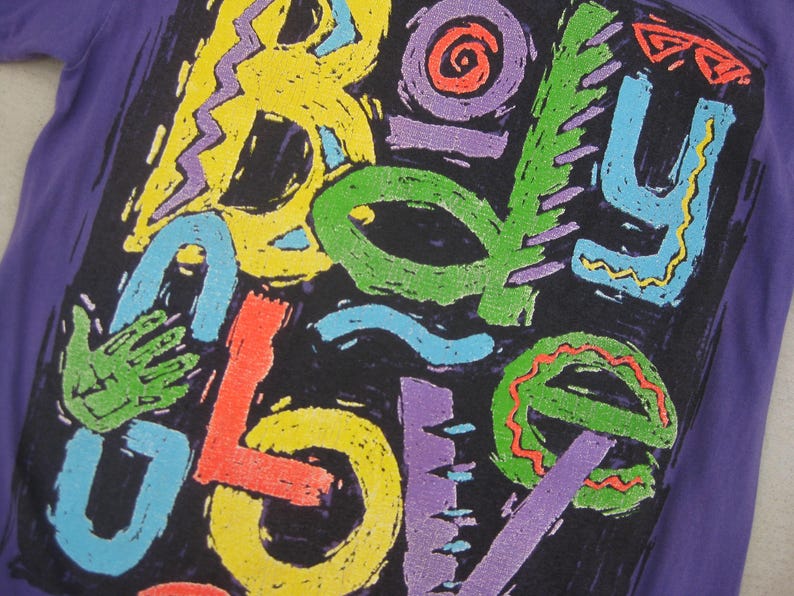 May include: Purple t-shirt with a colorful, abstract design. The design features the word "BOY LOVE" in various bright colors, including yellow, green, red, and blue, against a black background.