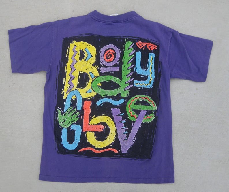 May include: A purple t-shirt featuring a colorful graphic design that reads "Body Glove" in a variety of bright colors. The design is set against a black background. The shirt has short sleeves and a crew neck.