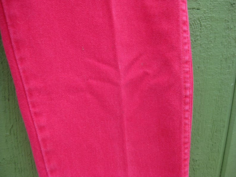 Peut inclure: Gros plan sur une section d'un pantalon en jean rose vif. Le tissu pr&eacute;sente une texture subtile et des coutures le long de la couture lat&eacute;rale. Le pantalon est d'une couleur unie et vibrante, sugg&eacute;rant un style d&eacute;contract&eacute;.