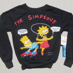 May include: Black crewneck sweatshirt featuring a graphic of Bart and Lisa Simpson. Bart is on a skateboard, and Lisa is jumping rope. The text "THE SIMPSONS" is in red above the graphic. Speech bubbles include "Gangway, Man!" and "Cut it out, Bart!"