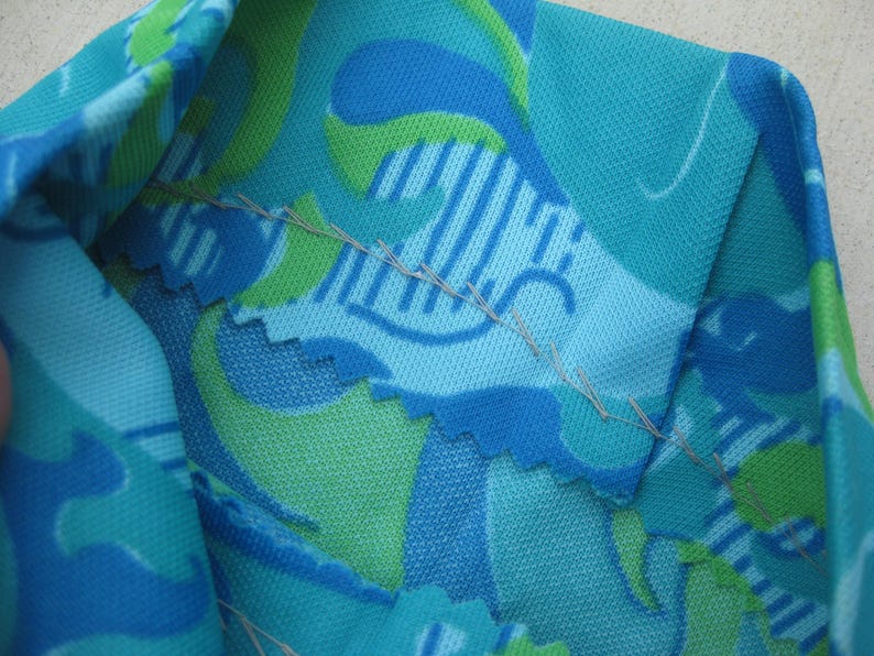 May include: Close-up of a section of fabric with a vibrant, abstract pattern. The design features shades of blue and green, with a textured appearance. The fabric is folded, revealing the stitching along the seams.