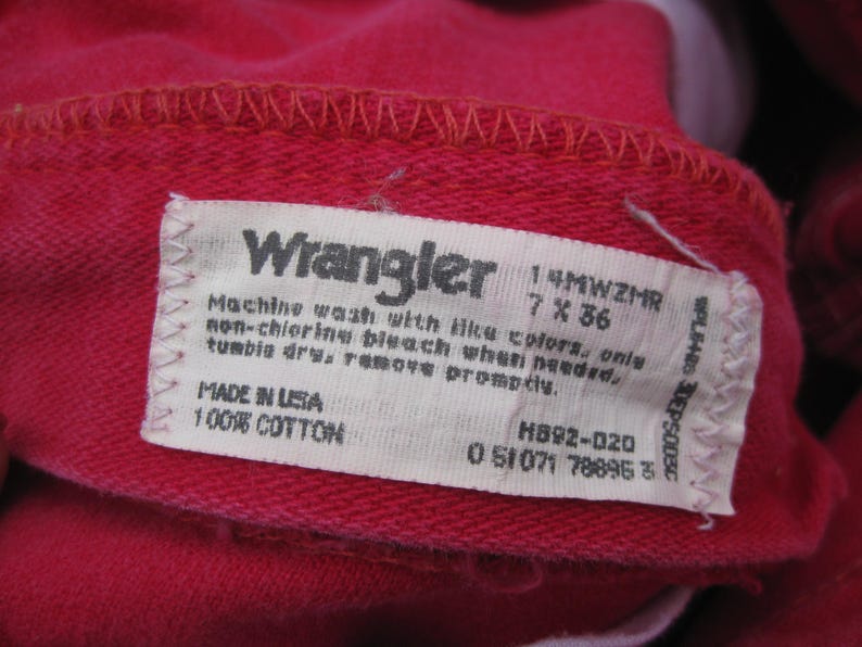Peut inclure: Gros plan sur un tissu rouge avec une &eacute;tiquette blanche. L'&eacute;tiquette indique "Wrangler" et comprend des instructions de lavage et des informations de taille: 7 x 36 pouces (17,78 x 91,44 cm). Fabriqu&eacute; aux &Eacute;tats-Unis, 100% coton.
