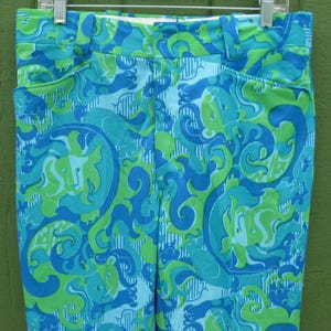 May include: A pair of high-waisted pants with a vibrant, swirling pattern in shades of blue and green. The pants feature a classic design with pockets and a waistband, hanging from a metal hanger.