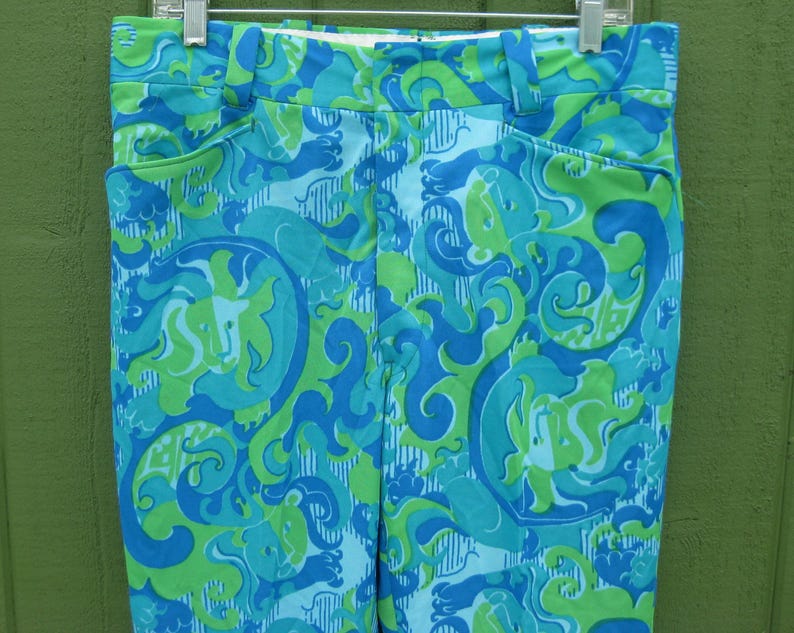 May include: A pair of high-waisted pants with a vibrant, swirling pattern in shades of blue and green. The pants feature a classic design with pockets and a waistband, hanging from a metal hanger.