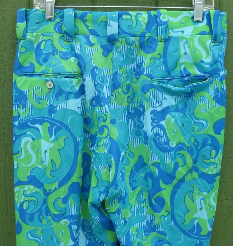 May include: A pair of vintage trousers with a vibrant, swirling pattern in shades of turquoise, blue, and lime green. The trousers feature a classic design with belt loops, pockets, and a button closure. The fabric has a slight sheen.