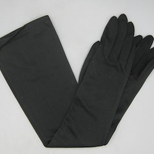 Peut inclure: Une paire de gants noirs opaques de longueur opéra, fabriqués dans un tissu lisse. Ces gants montent au-dessus du coude et présentent un design classique à cinq doigts avec des coutures apparentes et un ourlet droit au niveau de l'ouverture.