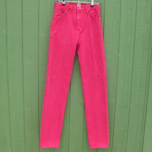Peut inclure: Un jean en denim rose vif suspendu &agrave; un cintre en m&eacute;tal. Le jean a une conception classique &agrave; cinq poches avec une taille haute et une jambe droite. La couleur est un rose vif et uni, et le jean semble &ecirc;tre en bon &eacute;tat.