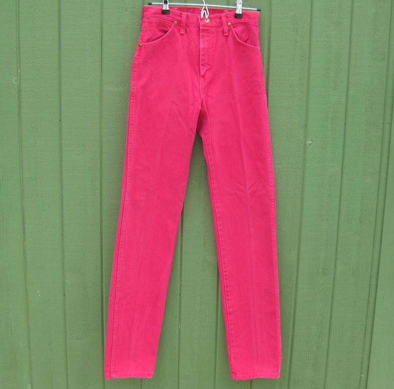 Peut inclure: Un jean en denim rose vif suspendu &agrave; un cintre en m&eacute;tal. Le jean a une conception classique &agrave; cinq poches avec une taille haute et une jambe droite. La couleur est un rose vif et uni, et le jean semble &ecirc;tre en bon &eacute;tat.