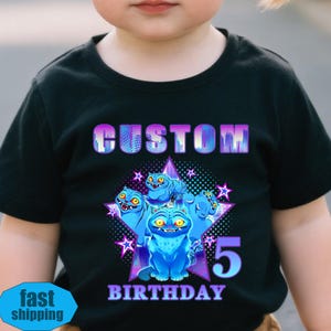 May include: Black t-shirt with a colorful graphic design. The design features blue cartoon creatures, a star, and the text "CUSTOM" and "BIRTHDAY 5". The shirt is made of a soft material.
