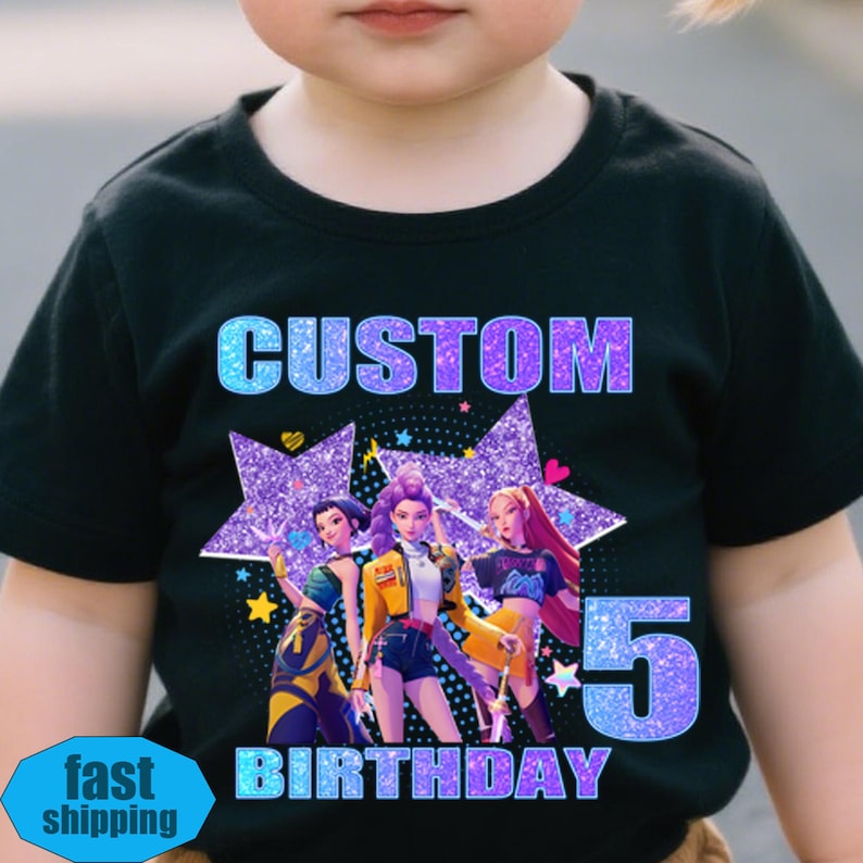 May include: Black t-shirt with a graphic design featuring three animated figures, stars, and the text "CUSTOM BIRTHDAY 5". The design has blue and purple glitter accents. The shirt is worn by a child.
