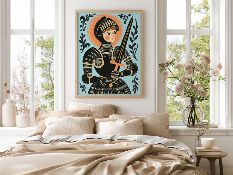 May include: A framed art print of a medieval knight in black armor, holding a sword. The artwork features a light blue background with an orange halo and decorative black foliage. The print is displayed above a bed with beige bedding.
