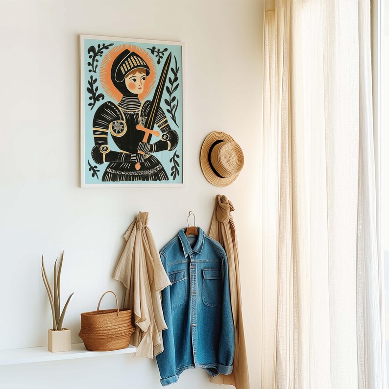 May include: A framed art print of a medieval knight in black armor, holding a sword, set against a light blue background with an orange halo. A straw hat and denim jacket hang on the wall below the artwork, along with a woven basket and a plant.