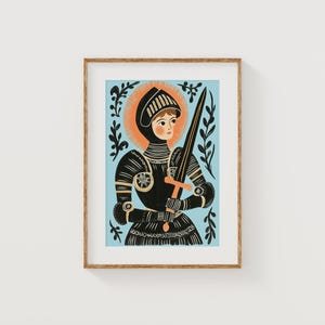 May include: Framed art print featuring a stylized illustration of a figure in black armor holding a sword. The figure has a halo and is set against a light blue background. The artwork is framed in a natural wood tone.