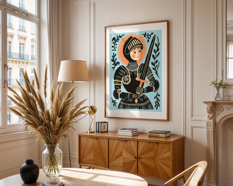May include: A framed art print featuring a stylized illustration of a figure in armor holding a sword. The artwork has a light blue background with black and orange accents. The print is displayed in a room with a wooden cabinet and a large window.