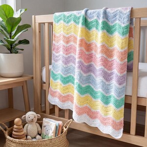 K&ouml;nnte beinhalten: Eine pastellfarbene H&auml;keldecke mit Wellenmuster, &uuml;ber ein Holzbettchen drapiert. Die Decke hat Streifen in Gelb, Rosa, Gr&uuml;n und Lila mit einem wei&szlig;en, gewellten Rand. Unter dem Bettchen befindet sich ein Weidenkorb mit Spielzeug.
